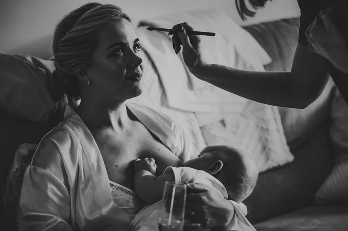 A bride holding a baby while her makeup is finished