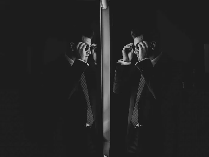 A groom reflected twice in a dark mirrored column