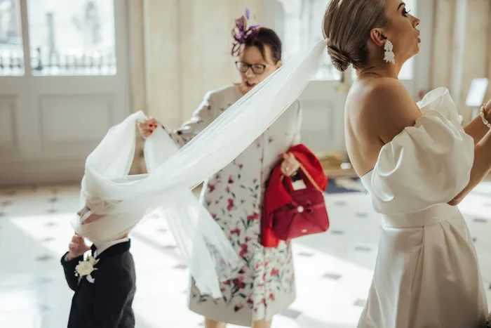 Two women lifting the bride’s veil while a small boy watches