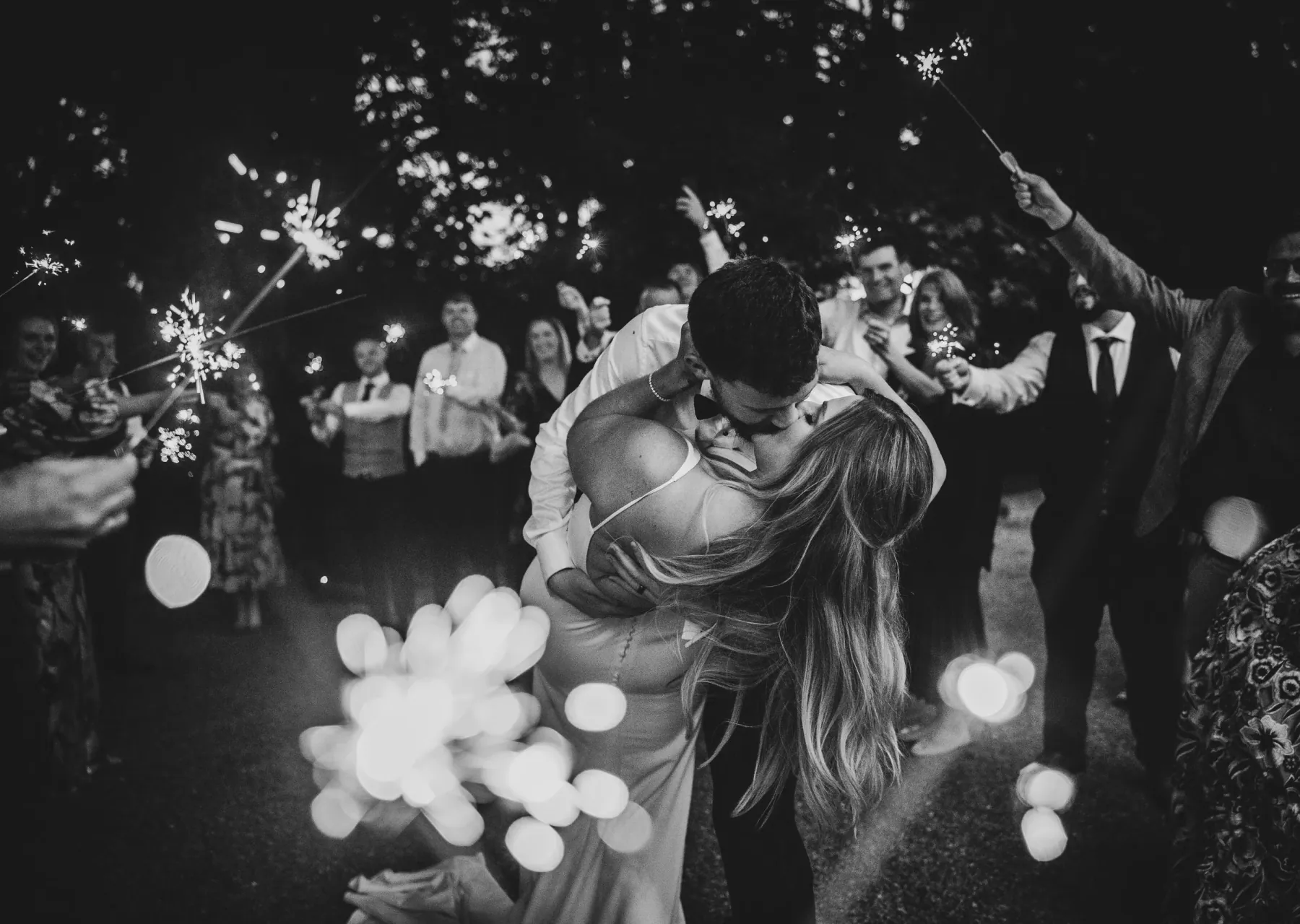A couple kissing as their guests hold sparklers around them