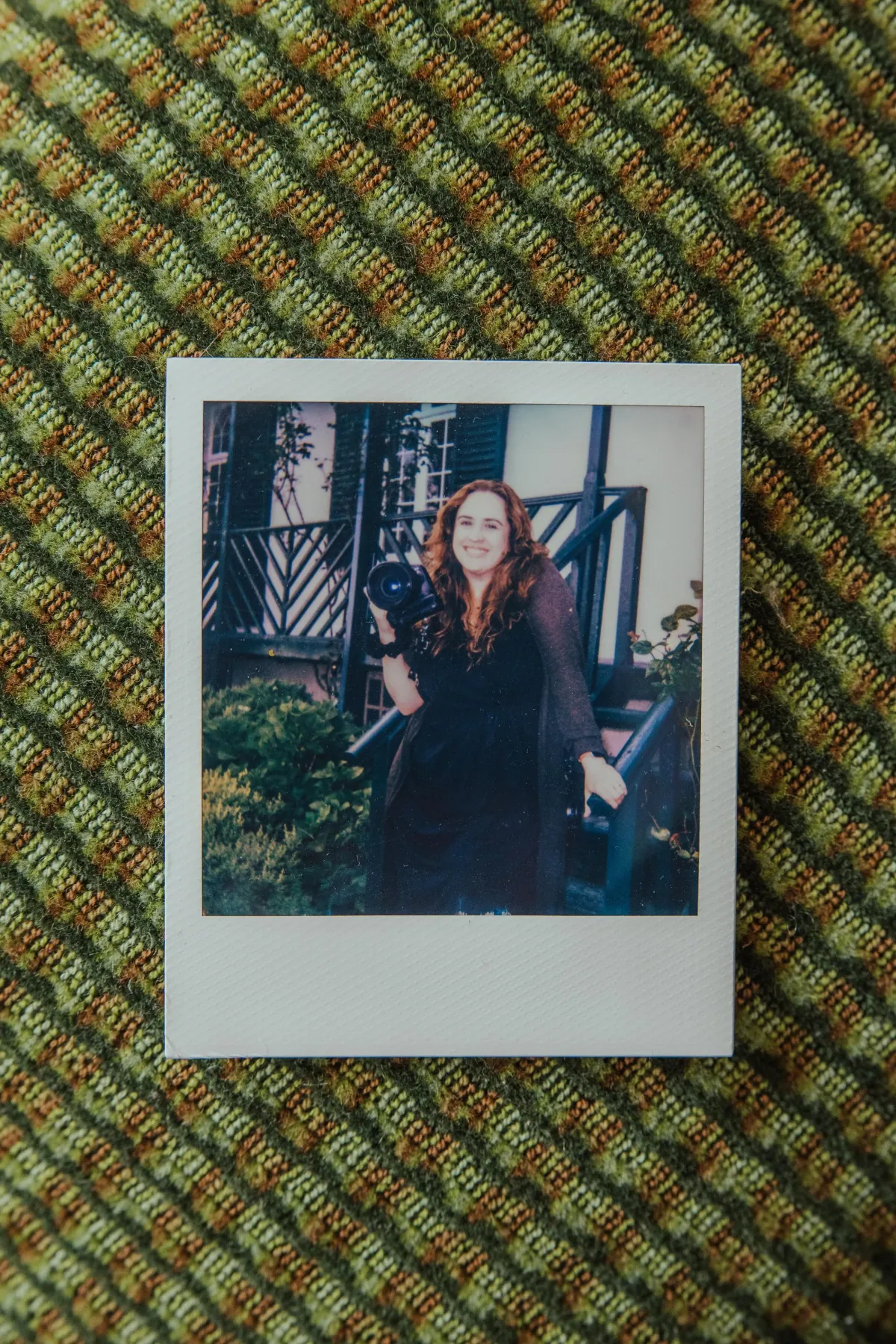 A polaroid of Lucy holding her camera, resting on a knitted blanket