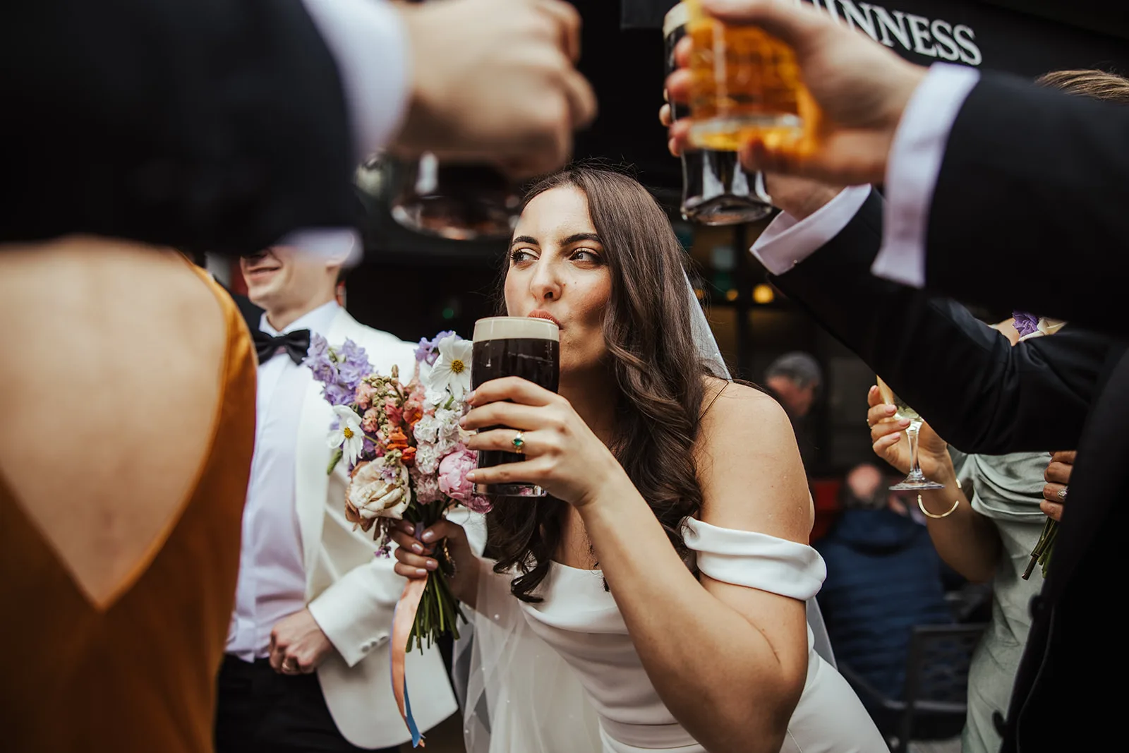 A bride drinking a pint of stout while her guests raise their glasses