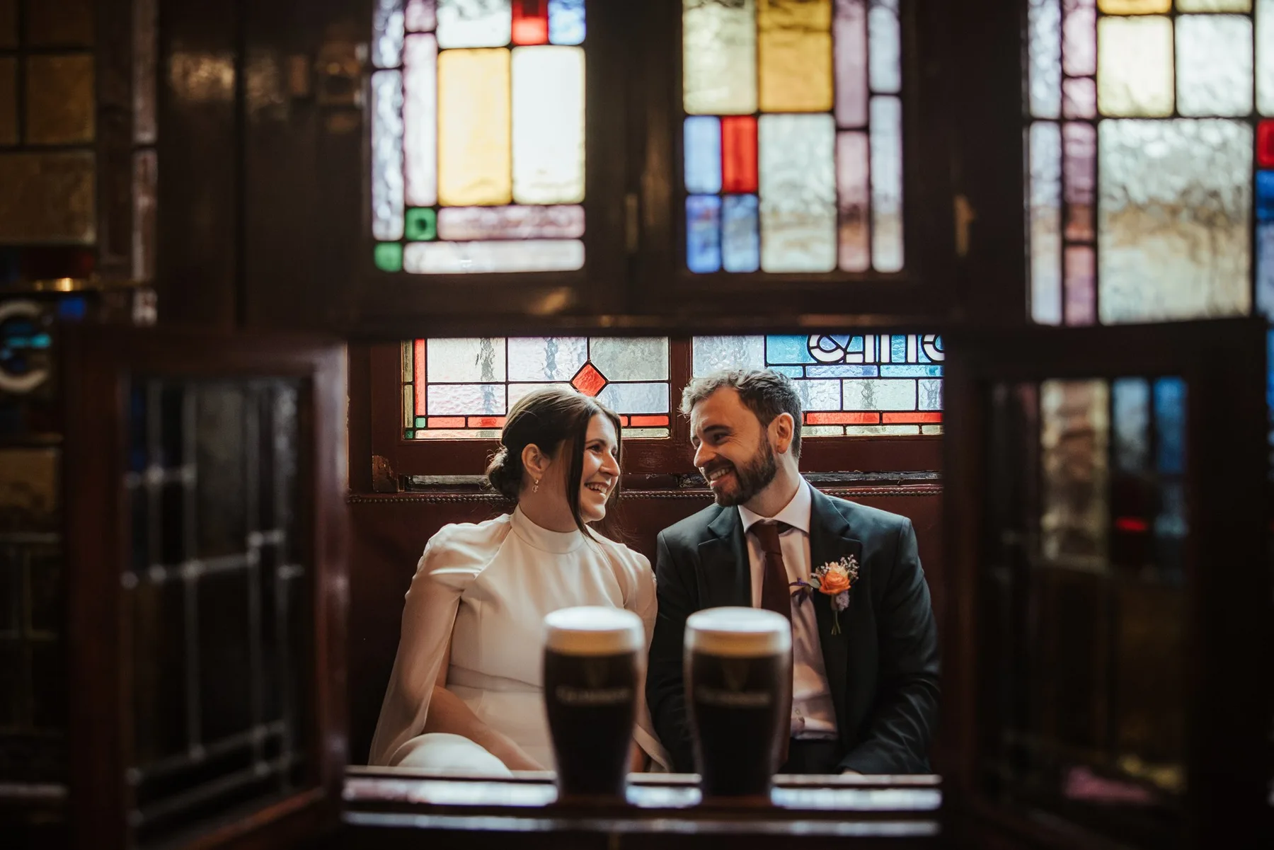 A couple in a pub snug with two pints and stained glass behind them