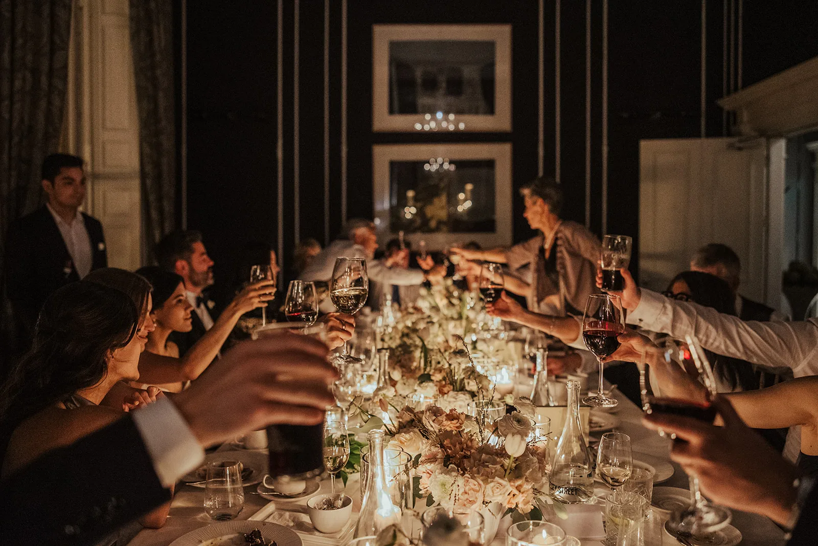 Guests raising their glasses along a long candlelit dinner table